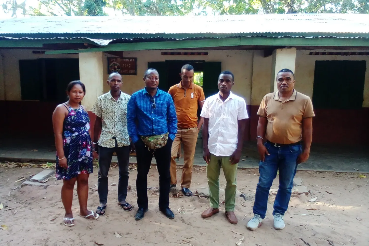A group of six teachers and community members stand outside a rural school building in Madagascar.