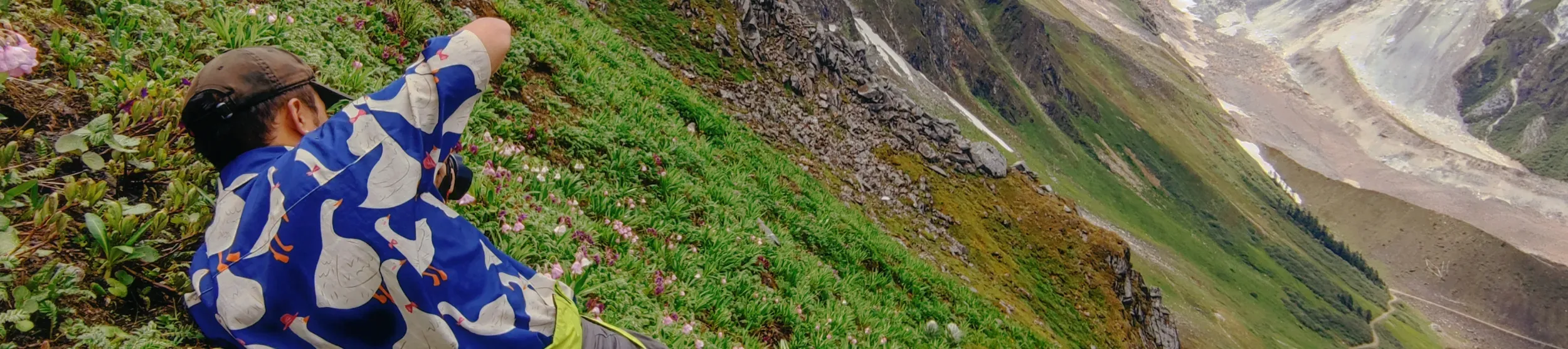 PhD student lays on mountain side taking a photo down the mountain 