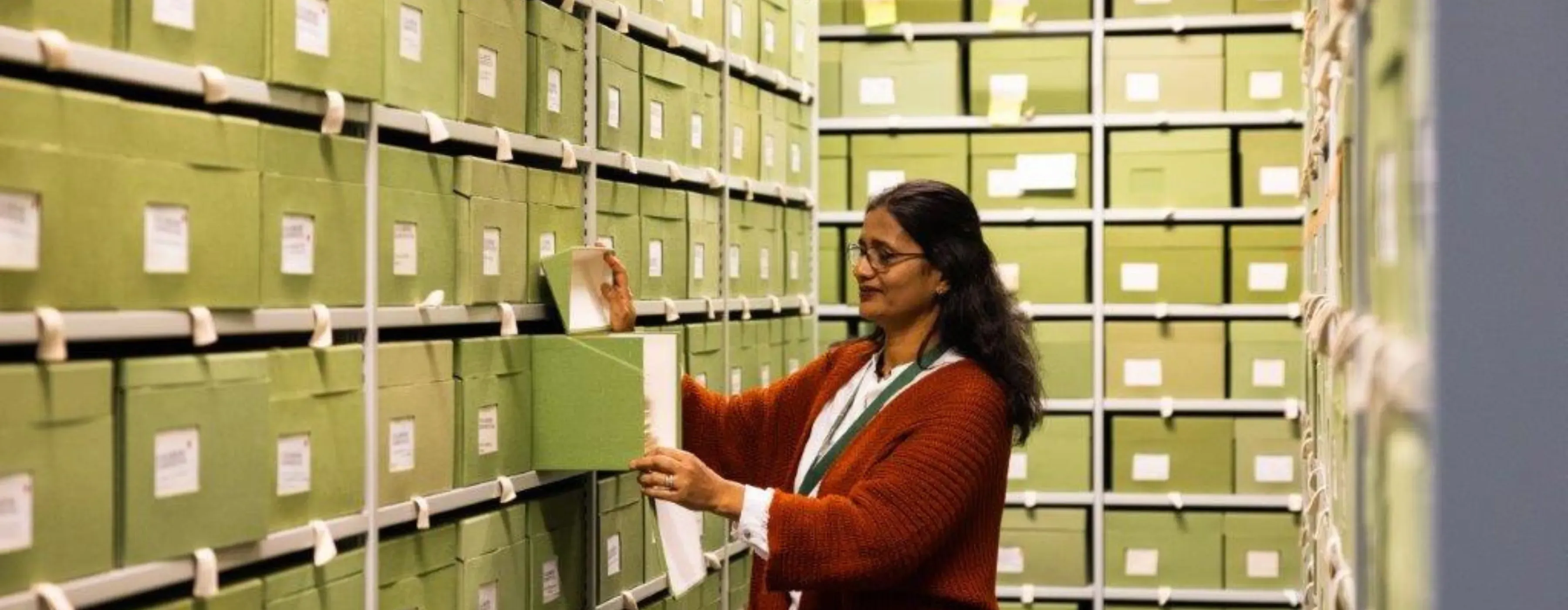 A woman selects a specimen box from a shelf filled with green archival boxes at Kew’s Fungarium.