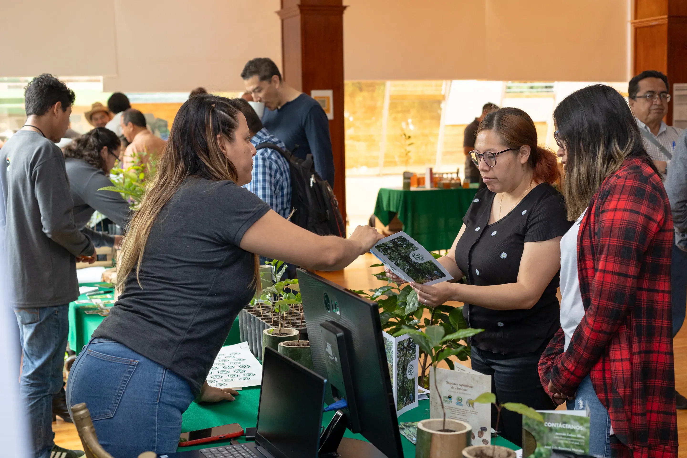 Three women stand around a counter covered in plants and a computer. One woman is talking to the other two about the contents of a training manual