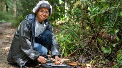 Malagasy woman in outdoor clothing, studying fungi specimens in a forest