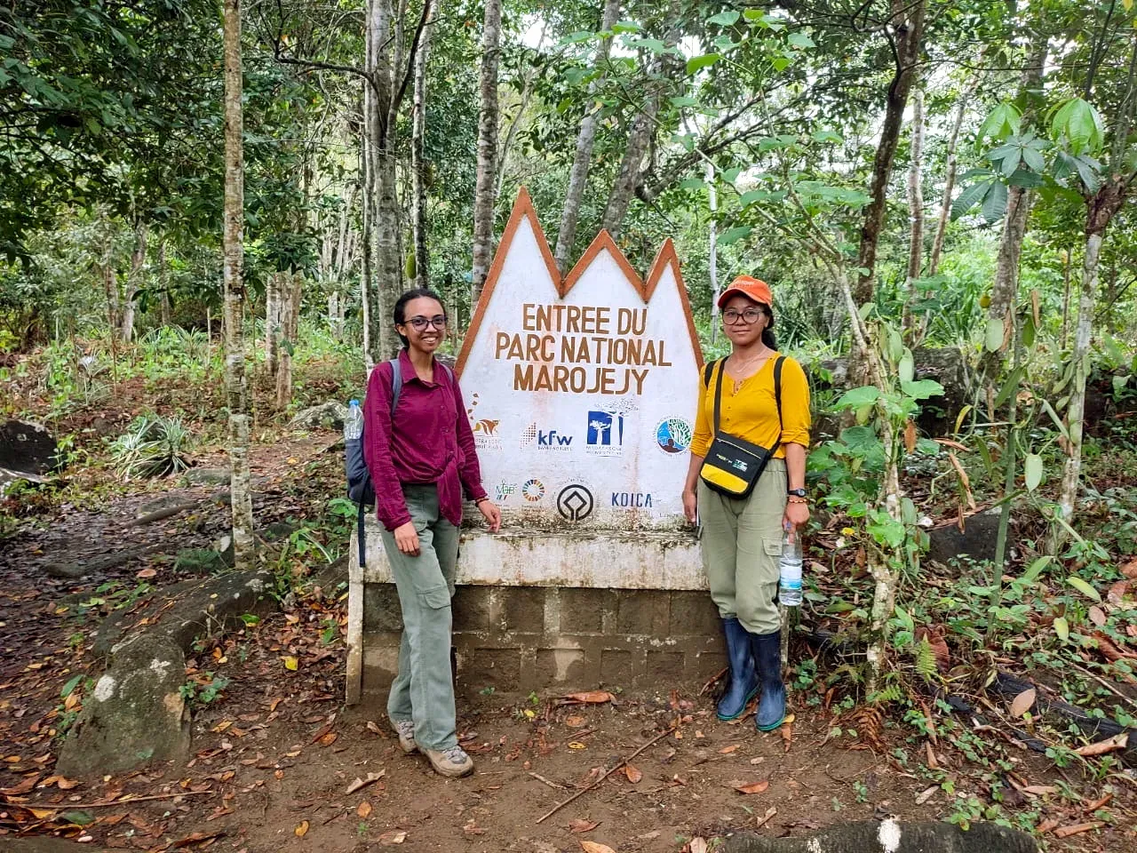 Two people standing either side of a large wooden sign in a forest