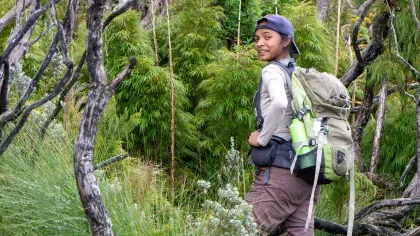 Lova, wearing a backpack, walking through trees and shrubs