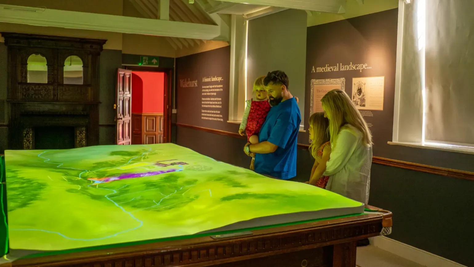 A family look at a green projection onto a table in a Mansion room at Wakehurst