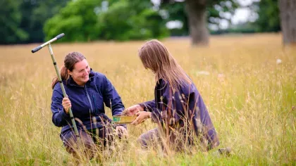 Two scientists sit in a meadow, holding a soil corer