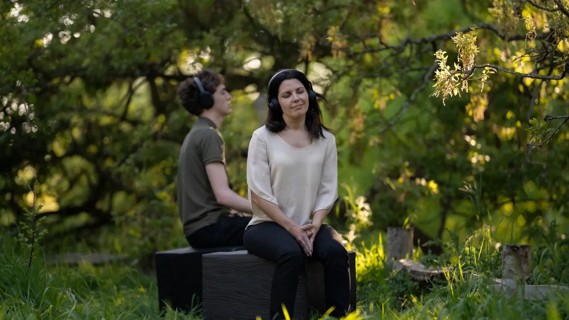Two people sitting with headphones and meditating in a forest