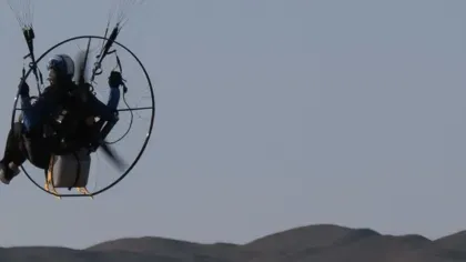 A person on a paramotor in the sky over faraway hills
