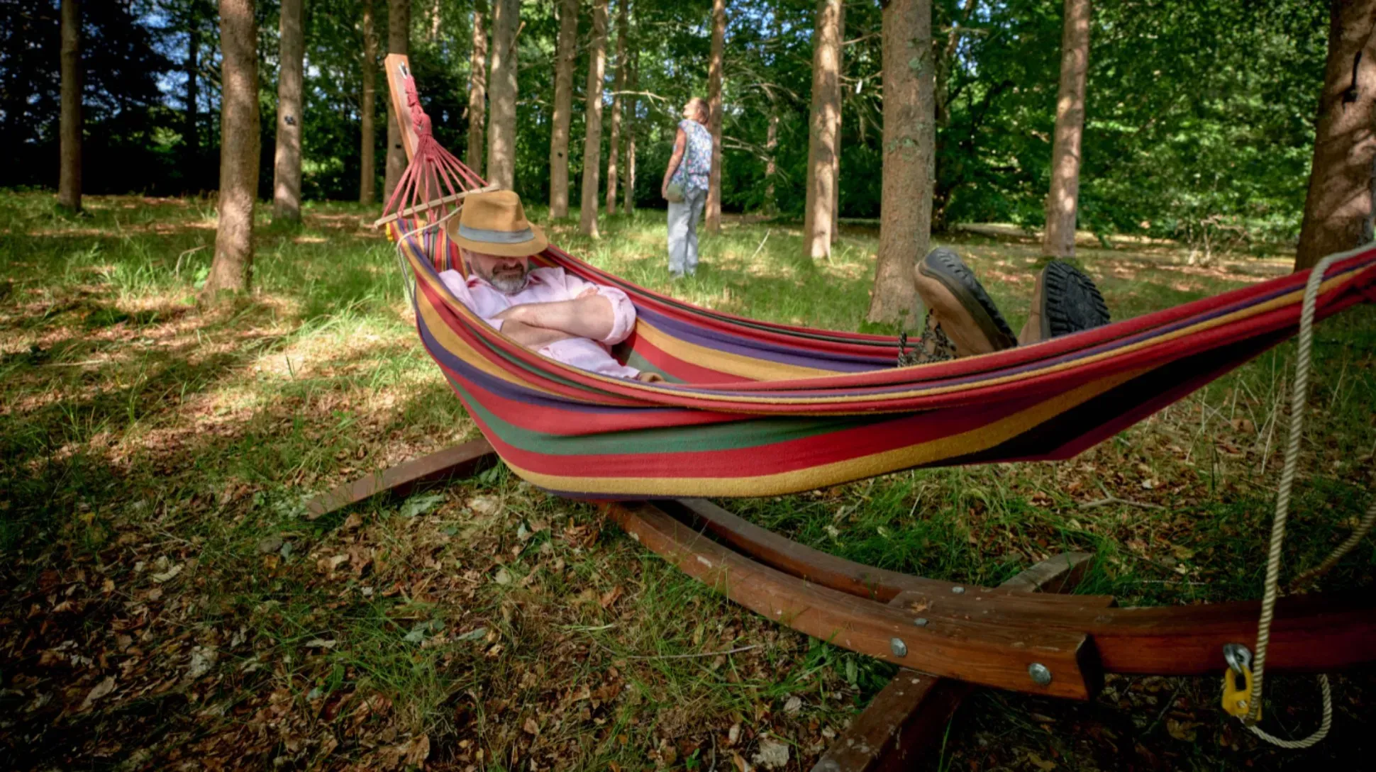 A person rests in a multicoloured hammock hung in a forest