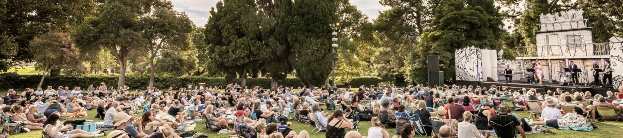 A large number of people sat on a lawn watching a theatre performance